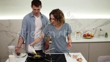 快乐的情侣一起做早餐。 女孩把混合鸡蛋从碗里倒进厨房炉子上的火锅里。 丈夫